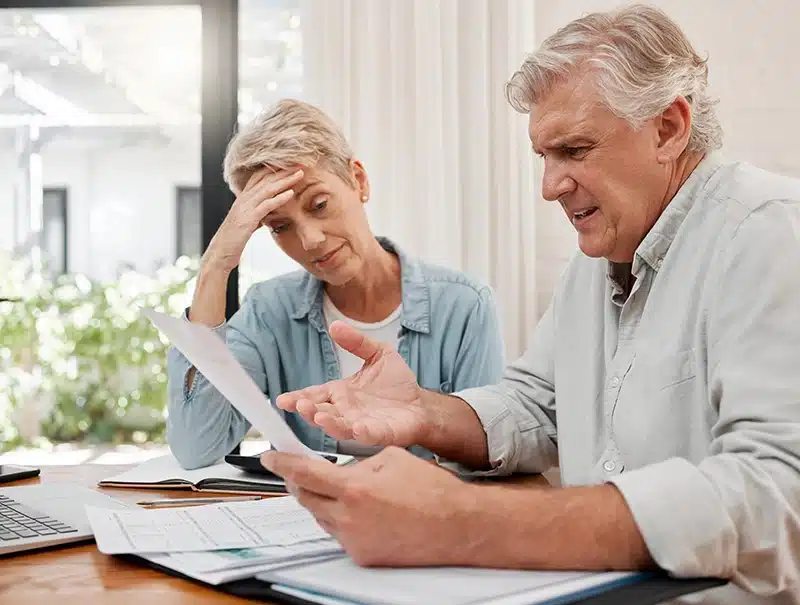 Older couple looking stressed while reviewing insurance documents at home