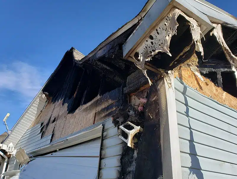 Severe fire and heat damage to the side of a residential garage after a gas-related incident