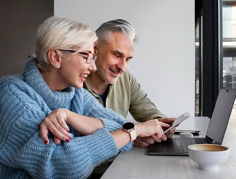 Happy older couple reviewing insurance claim progress on a laptop and phone