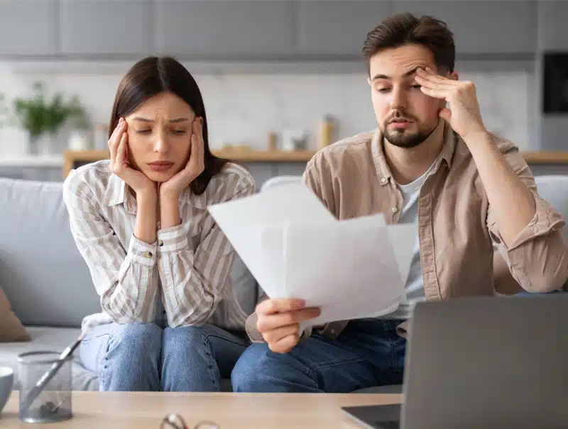 Young couple stressed and overwhelmed while reviewing insurance claim documents