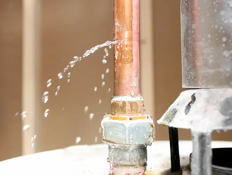 Close-up of a burst copper pipe leaking water inside a Connecticut home.