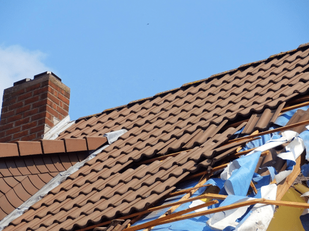Damaged tile roof with sections covered by a blue tarp.