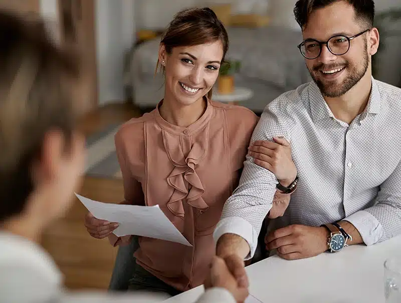 Smiling couple shaking hands with a claims adjuster during a consultation