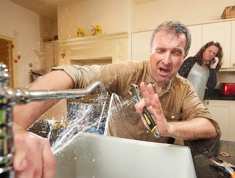 Man caught in an emergency plumbing situation with water spraying from sink