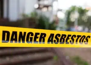 Yellow caution tape reading “DANGER ASBESTOS” blocking access at a home, indicating a hazardous materials area.