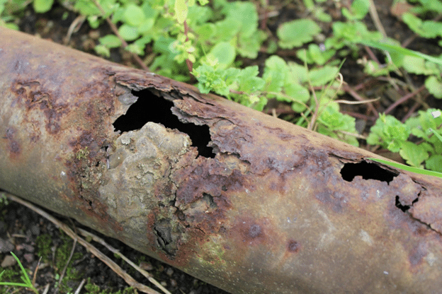 Rusted metal pipe with holes caused by corrosion and leaks.