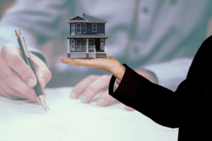Person holding a model house over a contract to represent property evaluation and protection.