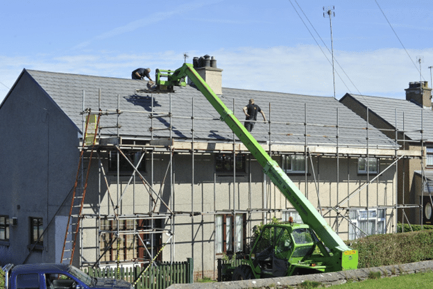 Construction crew repairing a residential roof using scaffolding and lift equipment.