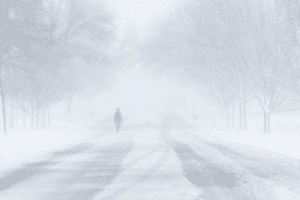 Person walking alone on a snow-covered street during a heavy winter storm.