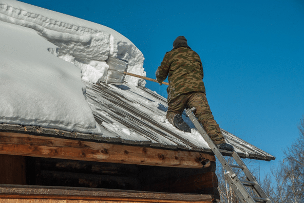 Homeowner clearing snow from a rooftop to prevent winter damage.