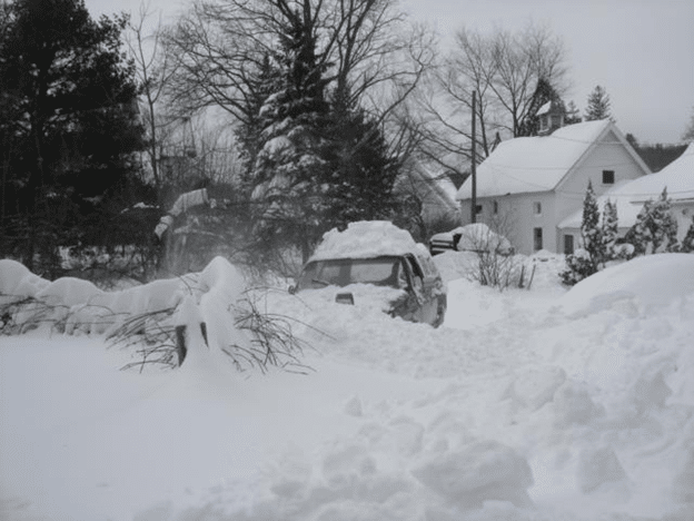 Snow-covered neighborhood with vehicles buried after a winter storm.