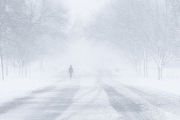 Person walking alone on a snow-covered street during a heavy winter storm.