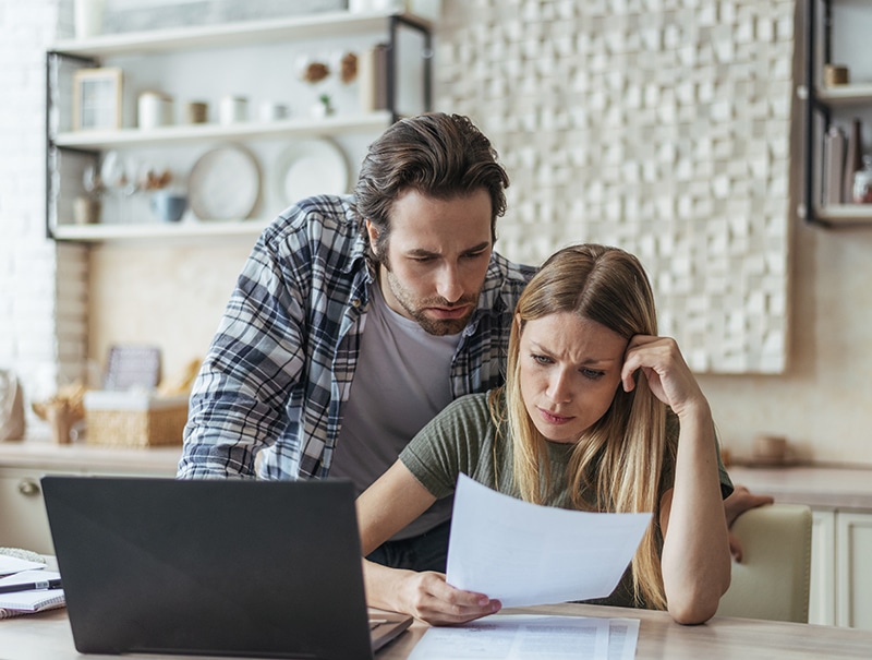 Homeowners looking over bills and insurance forms with worried expressions.