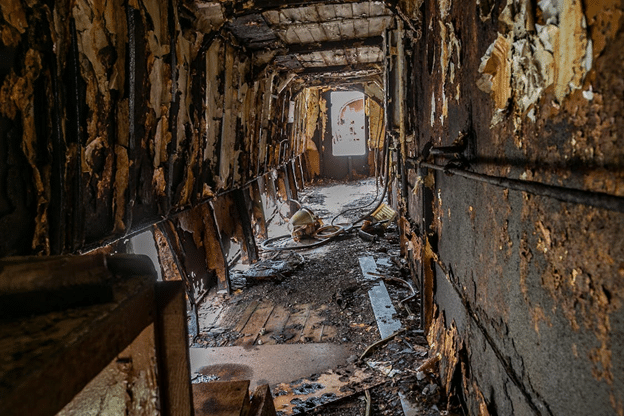 Heavily damaged hallway with burned and water-soaked materials after a disaster.