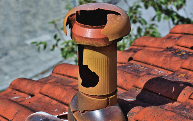 Hail-damaged metal chimney cap on a rooftop with visible structural cracks.