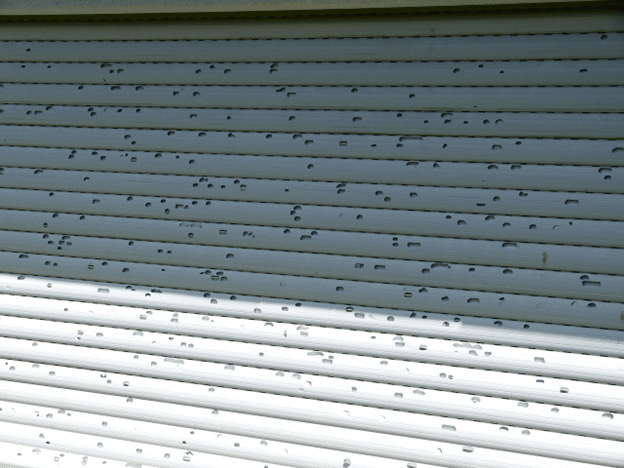 Exterior siding covered in dents caused by a hailstorm.